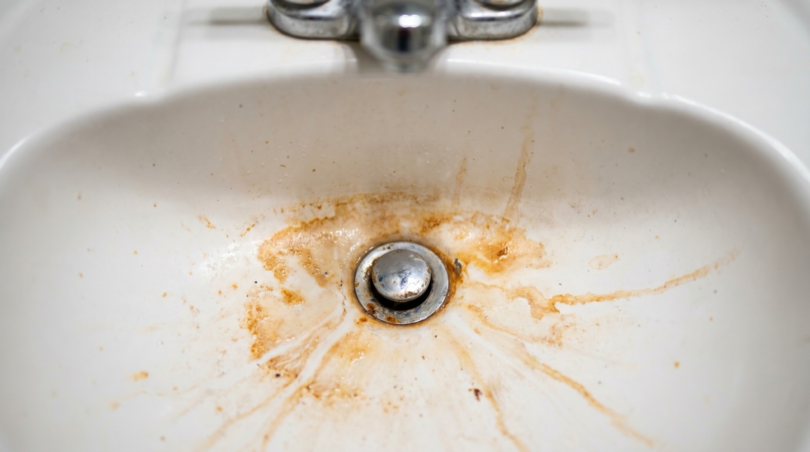 Orange iron stains ringing the drain of a white bathroom sink